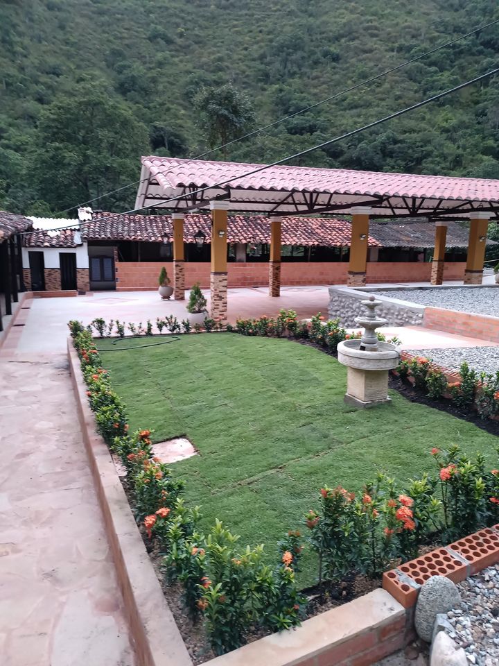 Jardín de finca con prado nuevo, fuente de piedra e ixoras naranjas junto al kiosco