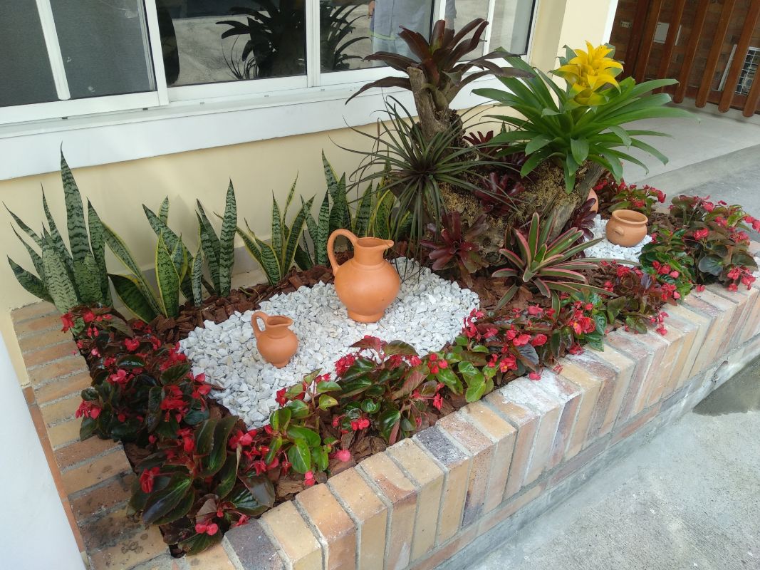 Jardinera de ladrillo con bromelias, lengua de suegra, begonias rojas y vasijas de barro
