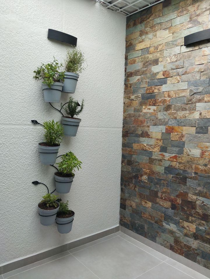 Materas grises con plantas aromáticas en un soporte de hierro sobre el muro
