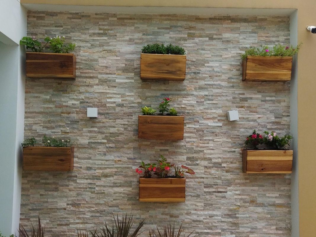 Muro de piedra con jardineras de madera flotantes llenas de flores